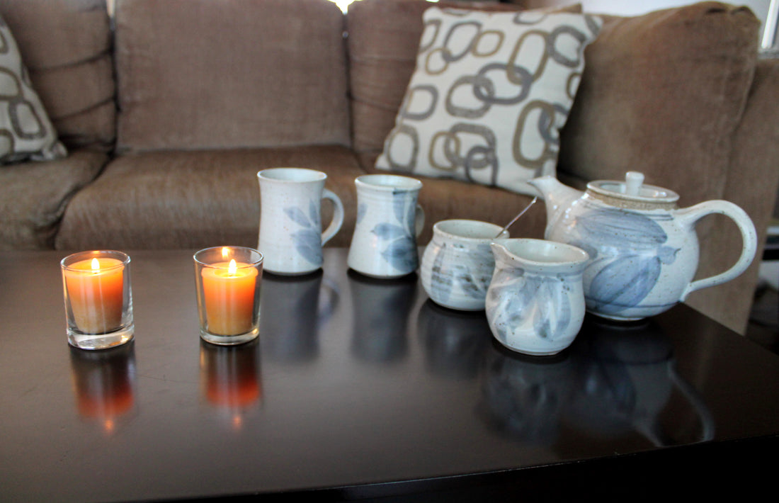 two beeswax votive candles burning on a coffee table beside a beautiful tea pot set